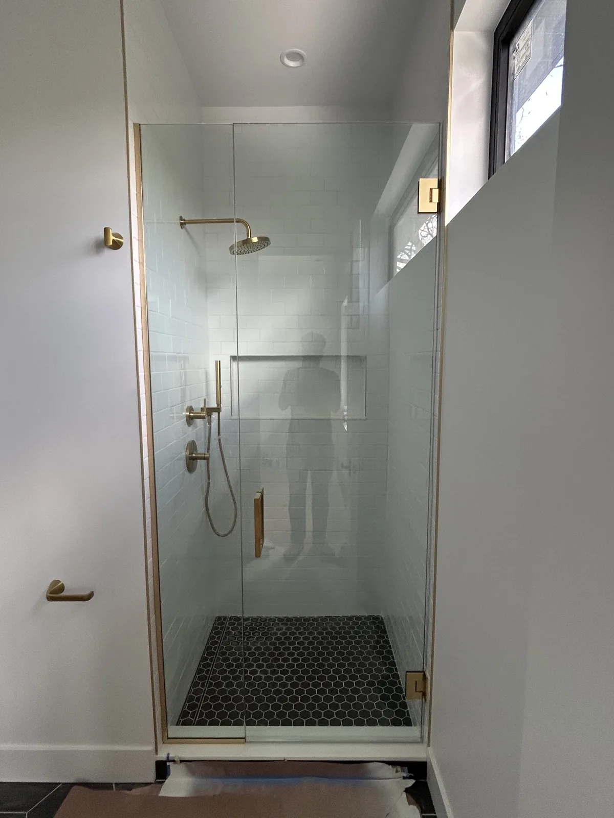 Glass shower with black hexagon mosaic pan and brushed-brass hardware