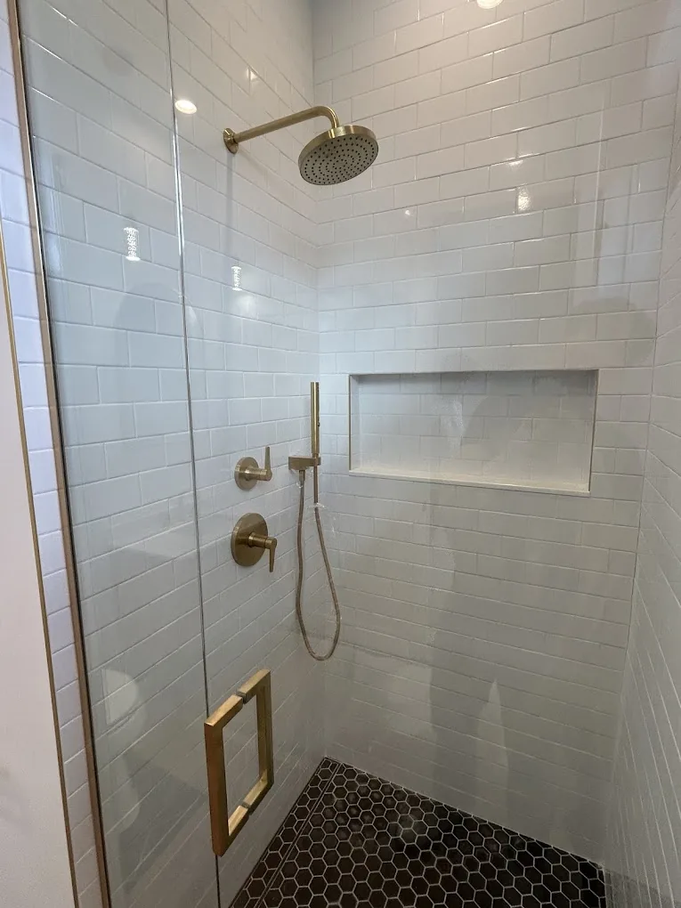 White tile shower with brushed-brass fixtures and black hexagon mosaic pan