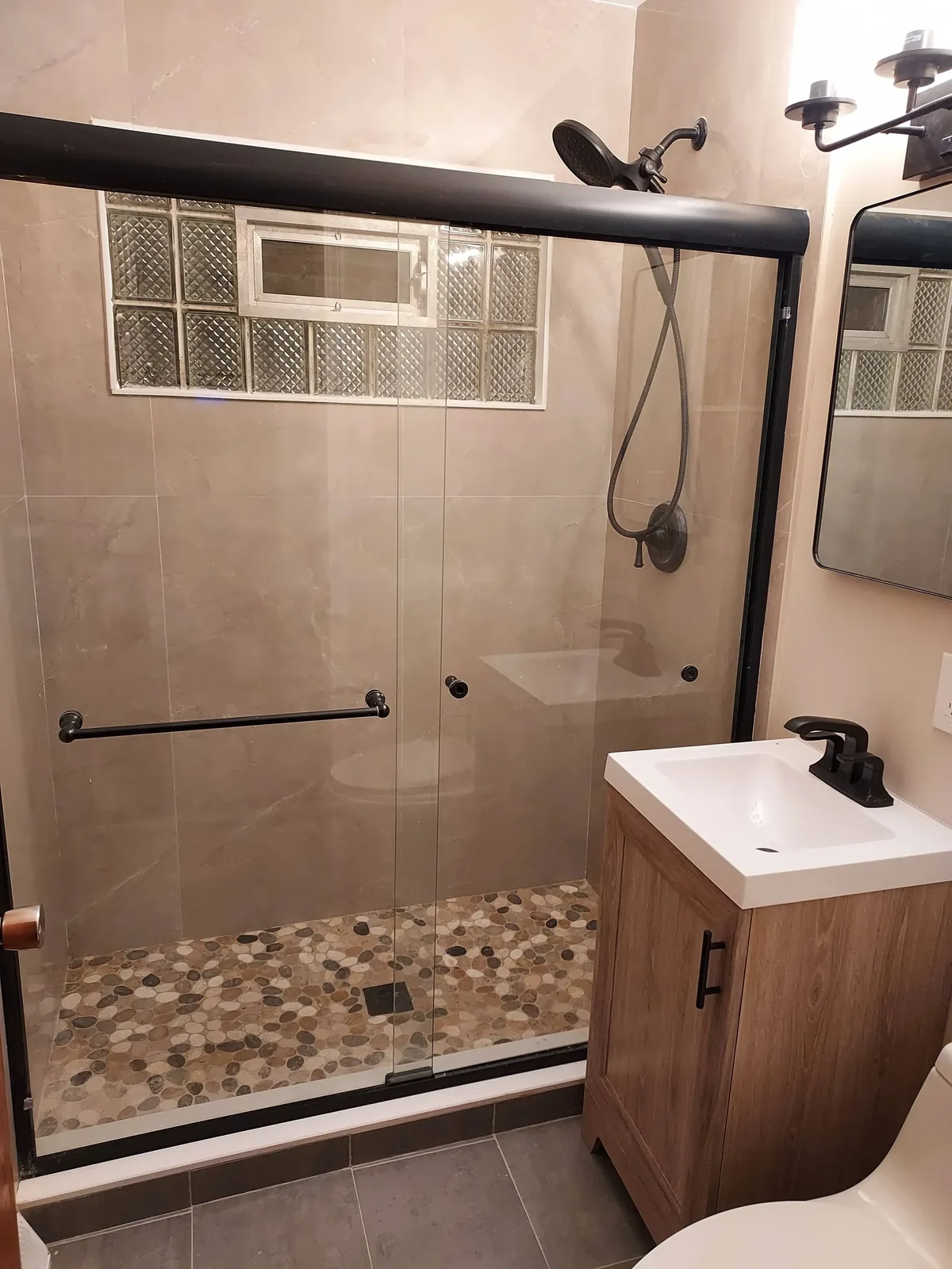 Bathroom with pebble-tile shower floor, bronze sliding door, and warm stone tile