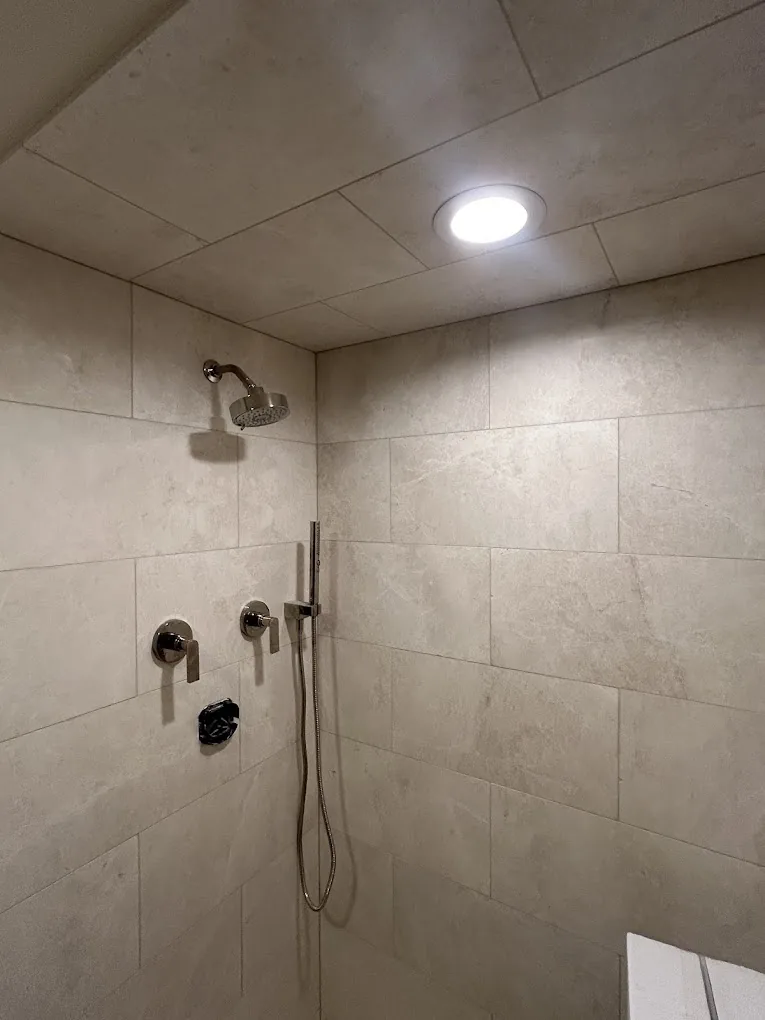 Large-format greige tile shower lit by a ceiling skylight