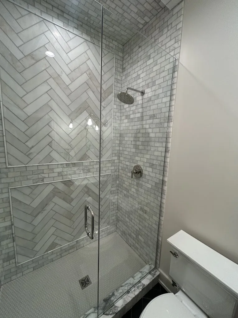 Herringbone marble shower with frameless glass door and slate herringbone floor