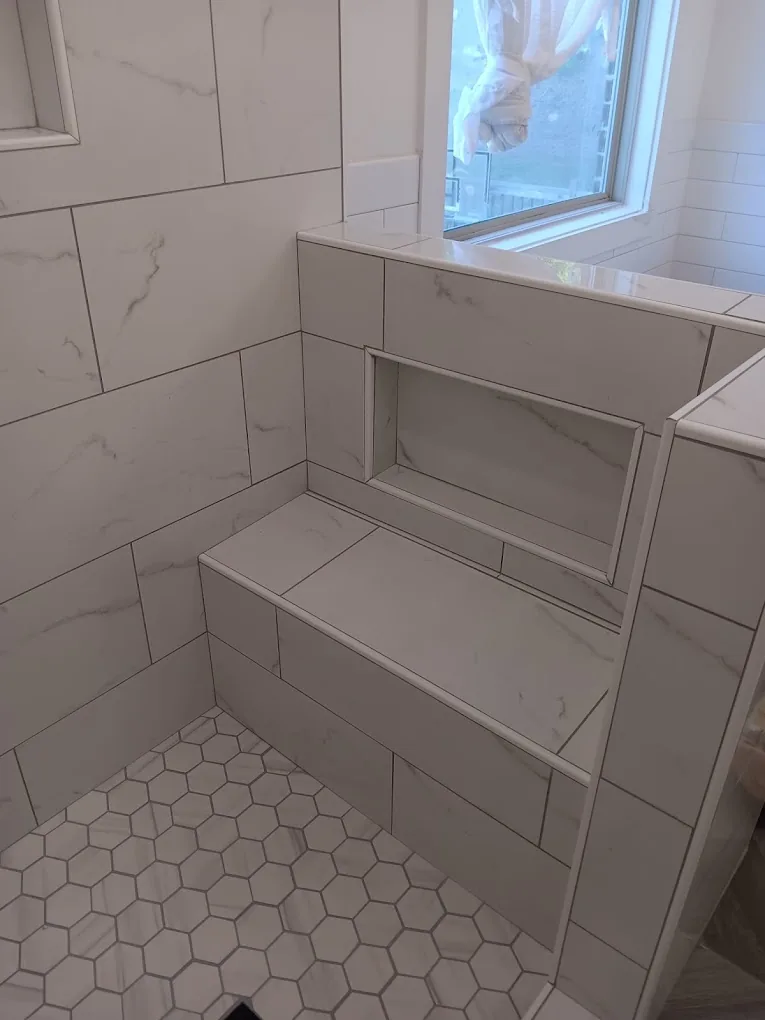 Marble-look shower with built-in bench, niche, and white hexagon mosaic floor