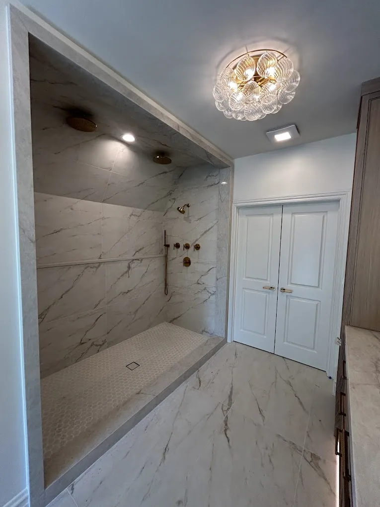 Marble walk-in shower with brass body sprays and a crystal ceiling fixture