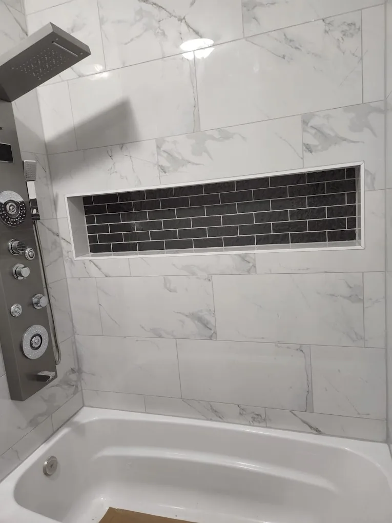 Tub with marble-look surround, dark subway niche band, and multi-jet spa shower panel