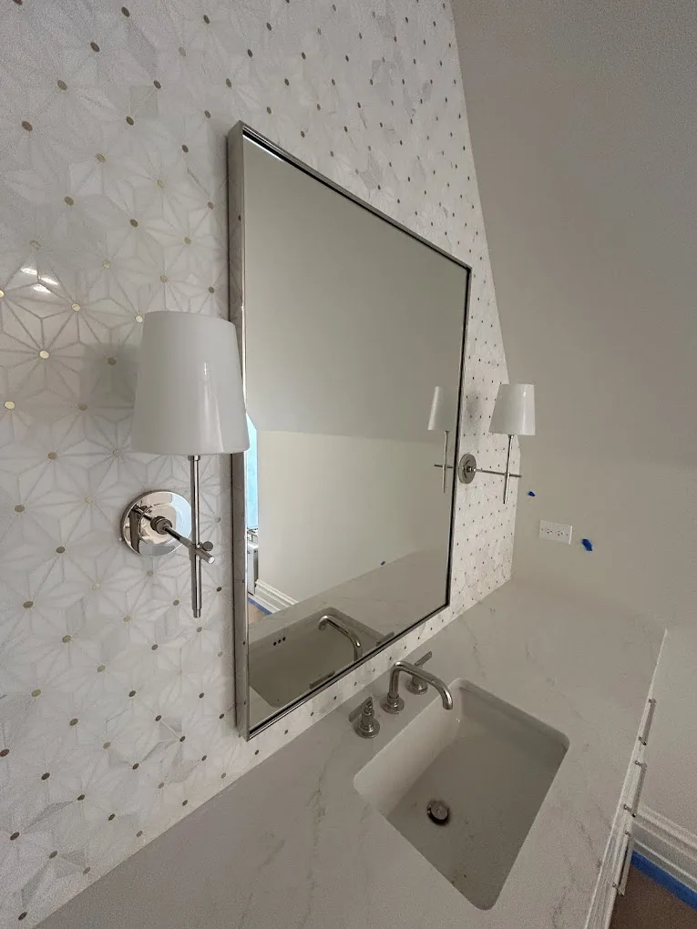 Vanity detail with black-framed mirror, sconce, and marble mosaic wall