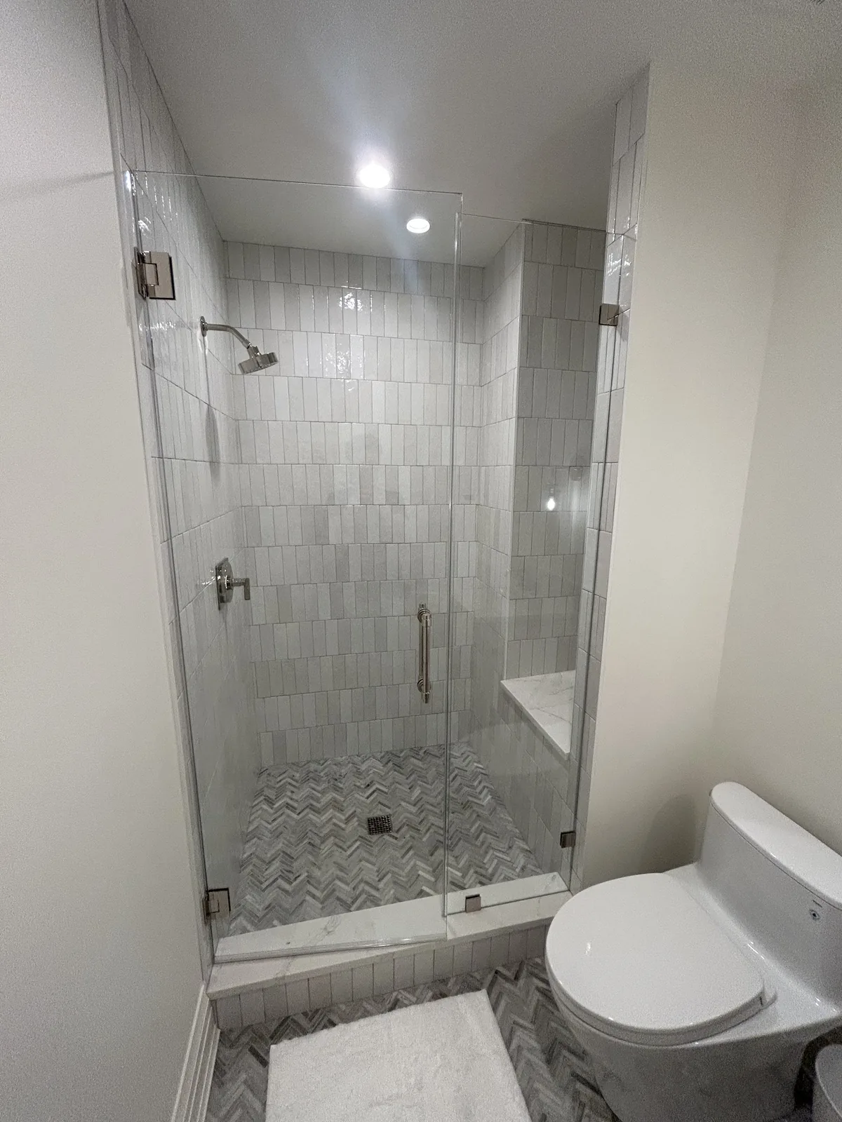 Curbed walk-in shower with marble-look walls, mosaic pan, and glass panel