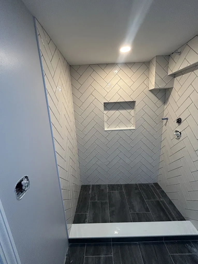 White herringbone tile shower with dark wood-look plank floor and bench