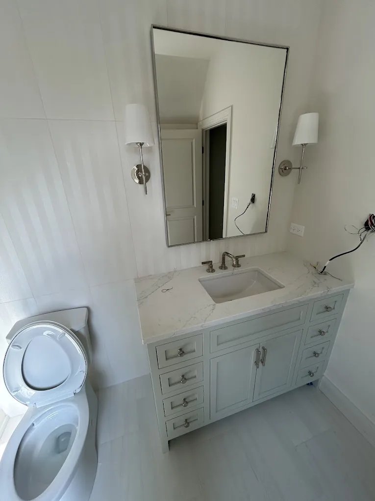 White shaker vanity with marble top, black-framed mirror, and double sconces