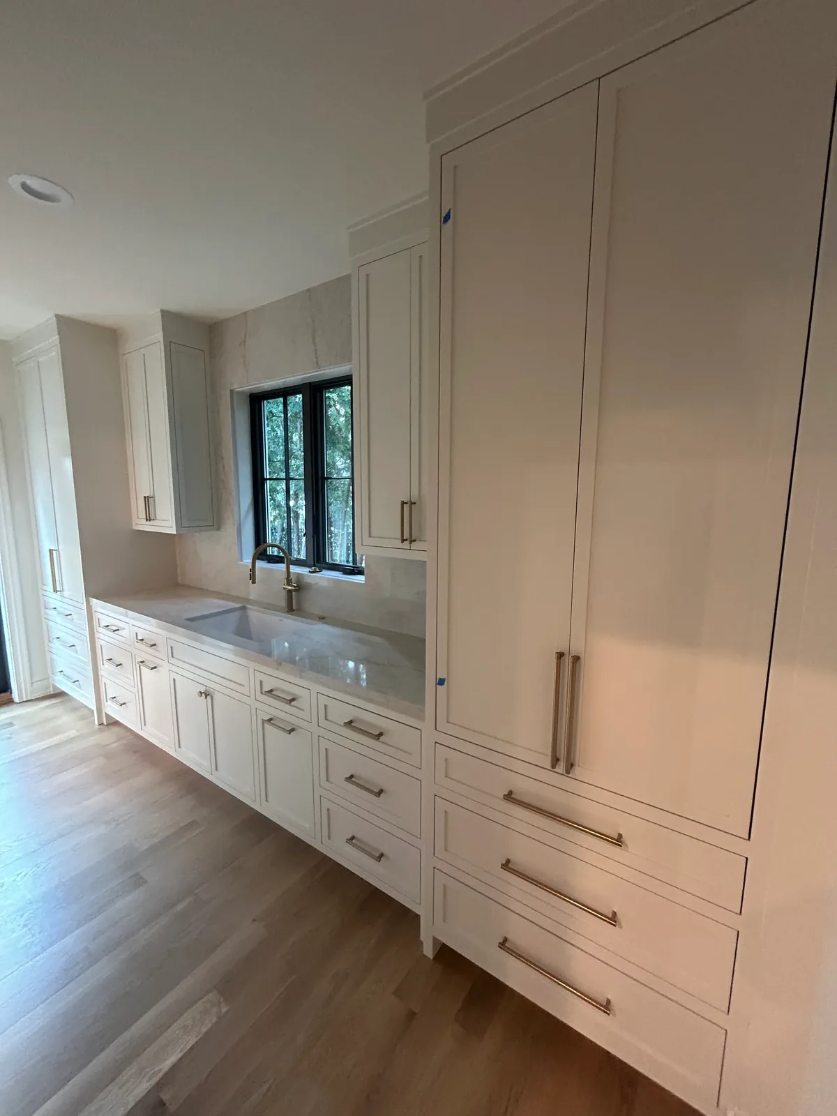 Inset-shaker kitchen run with brass hardware, stone slab backsplash, and black casement window