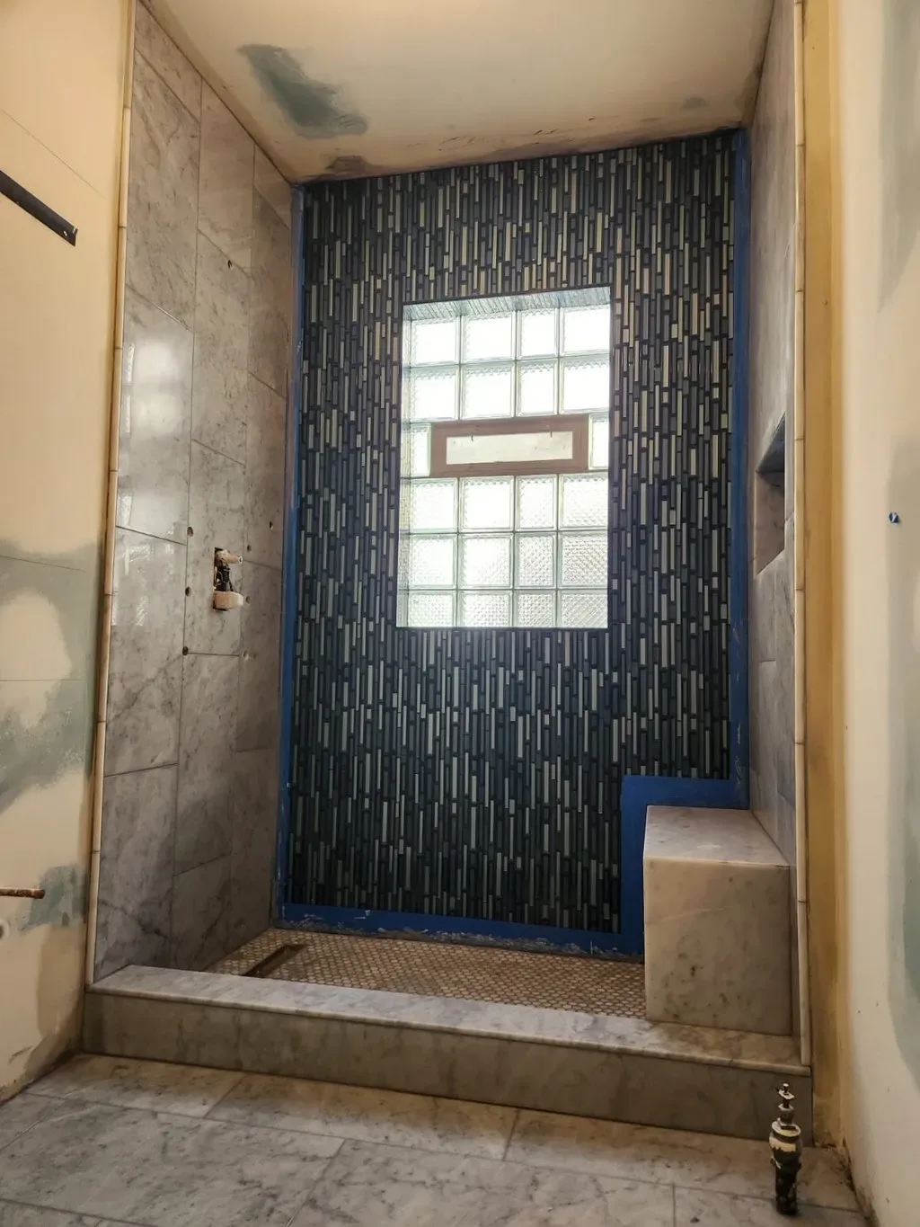 Blue glass mosaic accent wall being set in a marble shower surround